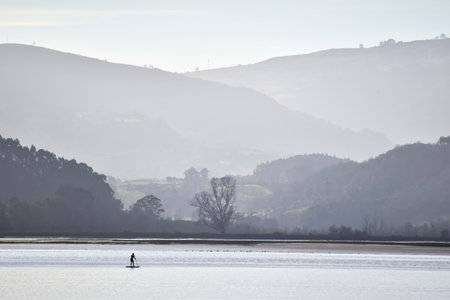 Panoramic view of the Villaviciosa estuary, with a figure in backlight, making snow between the misty mountains, in Asturias.の写真素材