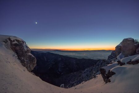 After sunset, the winter landscape illuminates the moon overlooking the distant cities from the...