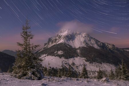 The moon shines on the mountain landscape in winter, star trails in the background