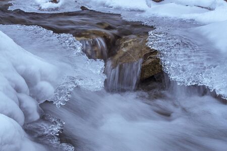 A clear mountain stream flows in the winter between frozen shores