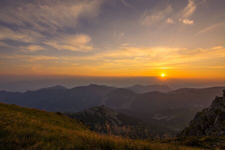 Sun rising from behind clouds in mountain landscapeの写真素材