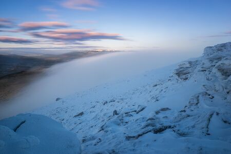 Low clouds and fog partly obscures the mountain ridge in winterの写真素材