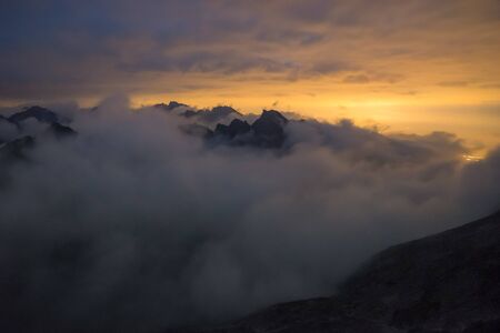 The valley is flooded in mist in a mountain environment. Over the fogs, only the high peaks of the...
