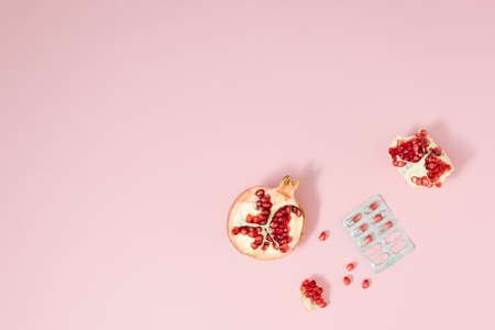 Pomegranate pieces on the pale pink backgorund, with grains inside a medicine packaging. Minimal concept.の写真素材