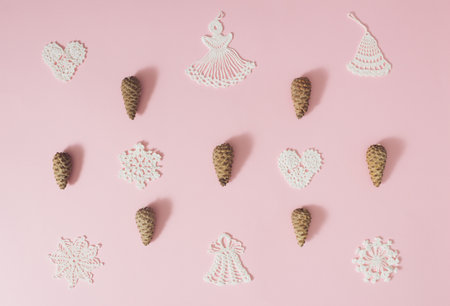 Crochet Christmas ornaments and pine cones on pale pink background. Minimal concept.の写真素材