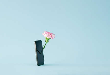 A smartphone with a pink flower (carnation) coming out of the screen on a blue background. Minimal...