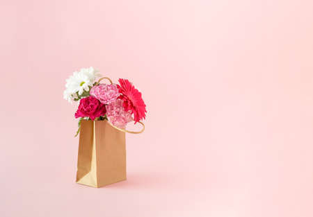 Fresh flowers in bloom packed in a brown paper bag on a pink background. Minimal concept.の写真素材