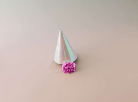 A party hat with a pink flower underneath, on a pink background. Minimal concept.