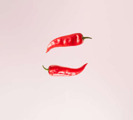 Two red peppers hovering in the air on a pink background. Minimal concept.の写真素材