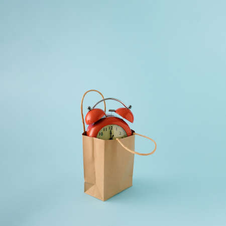 Red retro time clock in brown paper bag on blue background.