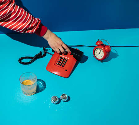 Minimal retro concept with hand answering red vintage phone on blue background. Retro futuristic...
