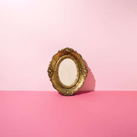 Vintage golden photo and picture frame leaning against pink wall. Minimal concept.の写真素材