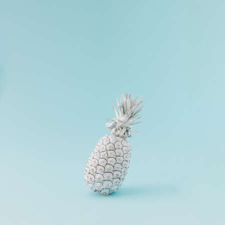 Pineapple colored in white balancing on blue background. Minimal summer concept.の写真素材