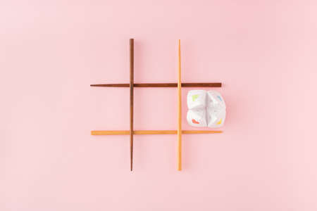 Tic tac toe game with wooden food chopsticks and paper origami fortune teller on pink background. Minimal concept.の写真素材