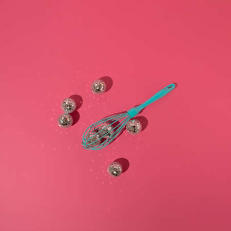 Turquoise egg mixer beater, manual cream mixing whisk with disco balls on pink background. Minimal concept.の写真素材