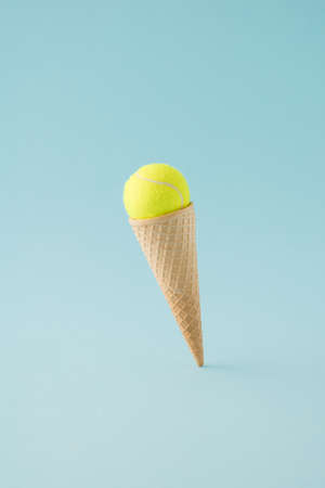 Ice cream cone with yellow tennis ball on floating above ble background. Minimal concept.の写真素材