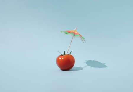 Fresh tomato with beach parasol on blue background. Colorful creative summer food concept.の写真素材