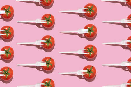 Seamless creative food pattern. Fresh tomatoes with white plastic forks on a pink background. Colorful food concept.の写真素材