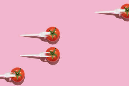 Creative food concept. Fresh tomatoes with white plastic forks on a pink background.