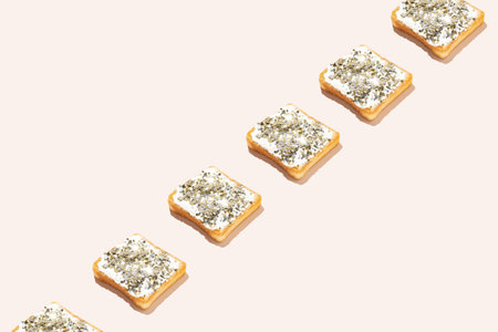 Slices of toasted bread spread with white cream and sprinkled with gold glitter arranged on pale pink background.の写真素材