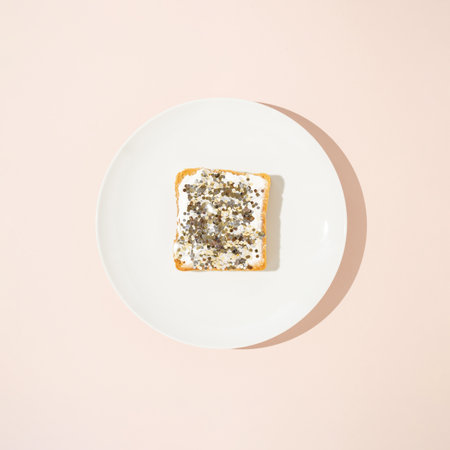 Slice of toasted bread spread with white cream and sprinkled with gold glitter on white plate.の写真素材