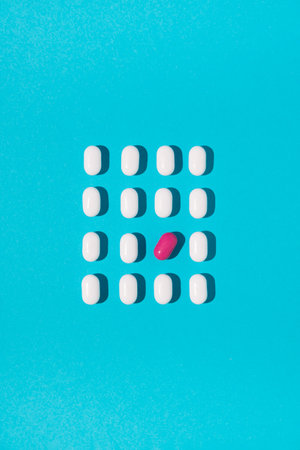 White pills with one tilted pink pill arranged on blue background. Flat lay. Minimal medical...