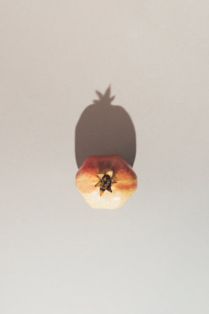Top view of fresh pomegranate on neutral grey background with sharp shadow. Minimal fruit concept.