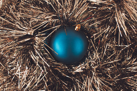 Blue shiny Christmas bauble on metallic golden foil tassels. Minimal greeting concept.の写真素材