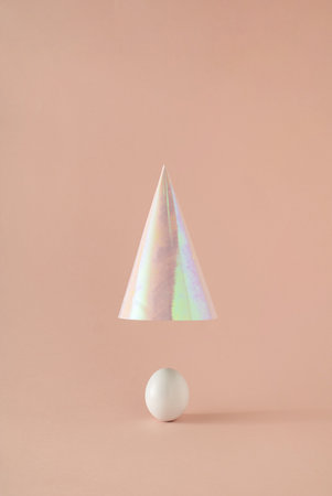 White Easter egg with party hat elevating above on pink background. Minimal concept.の写真素材