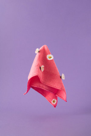 Pink dust cloth with fresh daiy flowers levitating against purple background. Spring cleaning concept.の写真素材