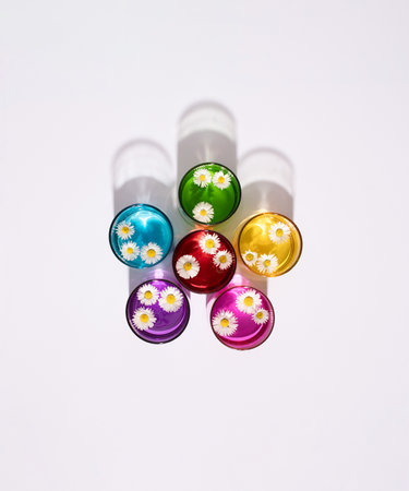 Rainbow colored drinking glasses filled with fresh daisy flowers on white background. Minimal spring and summer concept.の写真素材