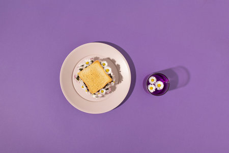 Toast sandwich filled with fresh daisy flowers served on plastic plate and drink on purple background. Minimal spring or summer concept.の写真素材