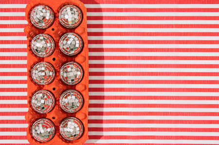 Shiny disco balls in red egg carton box on striped background. Minimal party concept. Flat lay. Copy space.の写真素材