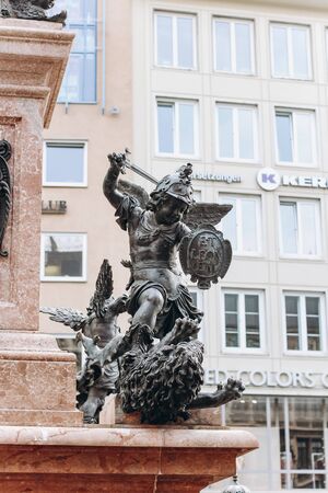Germany, Munich - September 01, 2013. Statue of putto killing a dragon on the Marian column's pedestal, Marienplatz with Spielzeugmuseum in backgroundのeditorial素材
