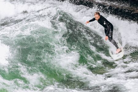 Germany, Munich - September 01, 2013. Atractive sporty man in neoprene shorty surfing on famous artificial river waveのeditorial素材