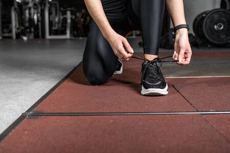 A girl ties her laces on sneakers in the gym close-up.