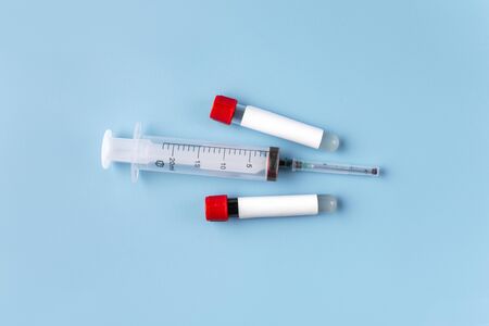 Two vacuum tubes for blood analysis with a blank label for inserting text and a syringe on a blue...