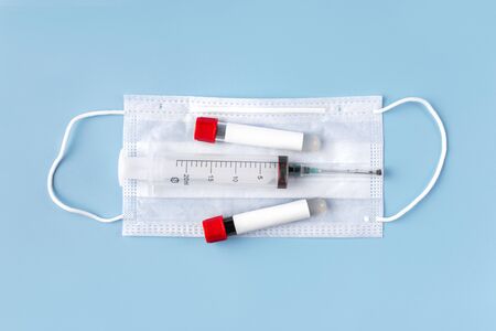 Two vacuum tubes for blood analysis with a blank label for inserting text, a mask and a syringe on a blue background. The concept of a coronavirus or covid-19の写真素材
