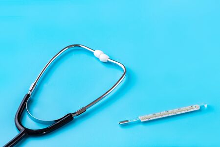 Stethoscope and glass thermometer for measuring body temperature on a blue background. Copy space....