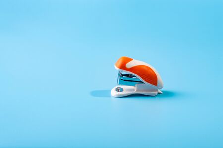 A small orange stapler in blue background. Close-up. Copy space. Space for textの写真素材