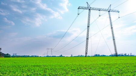 High voltage lines and power pylons in a green agricultural landscape on a sunny day with clouds in the blue sky.の写真素材