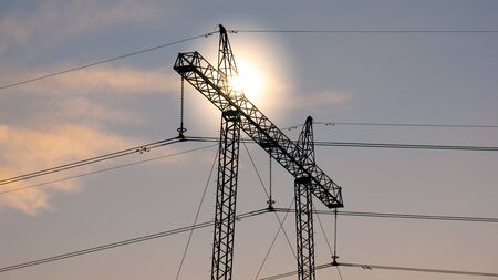 High voltage power transmission tower with the sun in the background