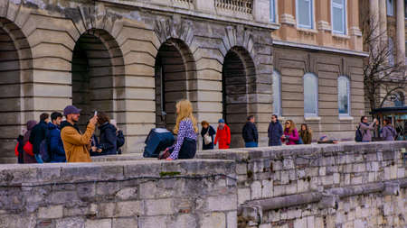 BUDAPEST, HUNGARY - 03 16 2019: Young man photographs his girlfriend in the Buda Castle.Around them tourists.のeditorial素材