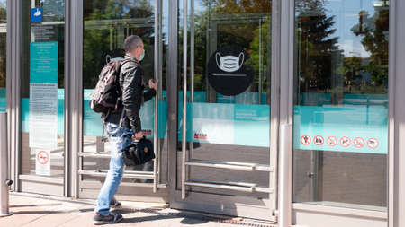 Gyor Hungary 05 21 2020: A man enters a shopping center in a mask. There is a warning sign at the entrance of the shopping center to wear a mask.のeditorial素材