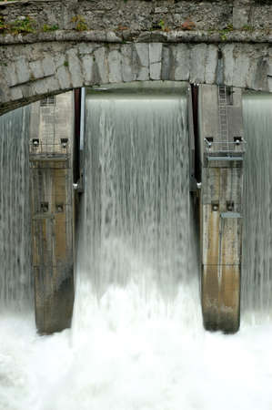 Detail of a dam on the river Simme in the Bern canton in Switzerland. The picture shows the powerful waters flowing from the dam and shot from underneath an old bridge's arch.の写真素材