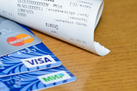 Plastic cards of VISA, Mastercard and MIR payment systems near the receipt as a purchase confirmation on brown background. Russia, Volgograd region, 14 March 2017のeditorial素材