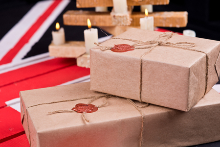 Boxes, wrapped into craft paper, fixed with packthread with a wafer on a background of a wooden candlestick on a coloured wooden desk.の写真素材