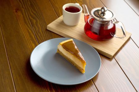 Transparent teapot with hot tea on the stand along with chocolate cheesecakeの写真素材