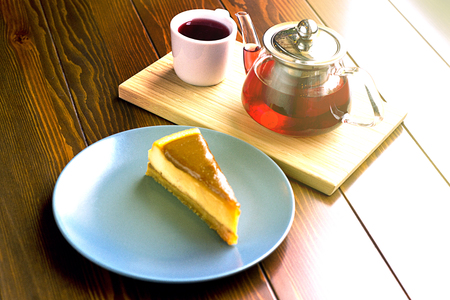 Transparent teapot with hot tea on the stand along with chocolate cheesecakeの写真素材