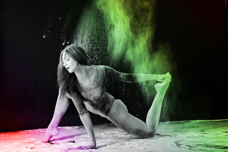 Slender girl dancing in white dust, Studio shot. Illuminated with colored lanterns. Blue and mustard on black backgroundの写真素材